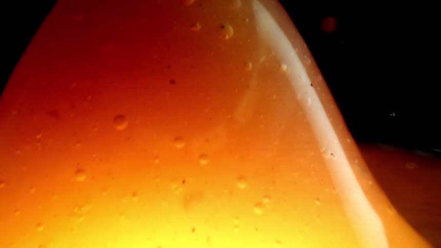 Translucent orange liquid with scattered bubbles illuminated against a dark background