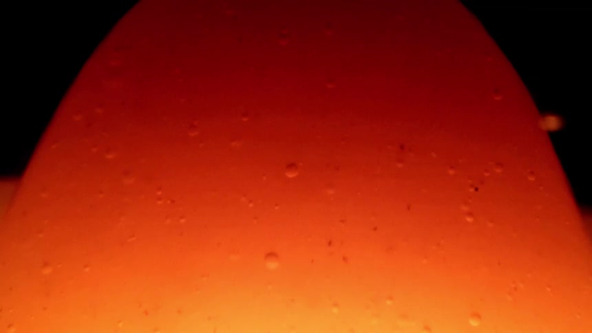 A vibrant orange semi translucent blob with small bubbles slowly rising and changing shape against a dark background resembling a lava lamp
