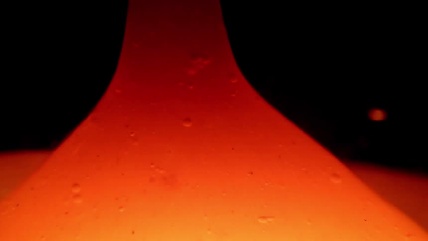 A vibrant orange mass of viscous liquid pulls upward into a tall thin pillar against a black backdrop the glowing material contains small internal bubbles and exhibits a slow rhythmic movement