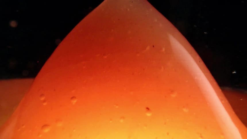 Orange liquid forming a dome with a raised central bubble against a dark background