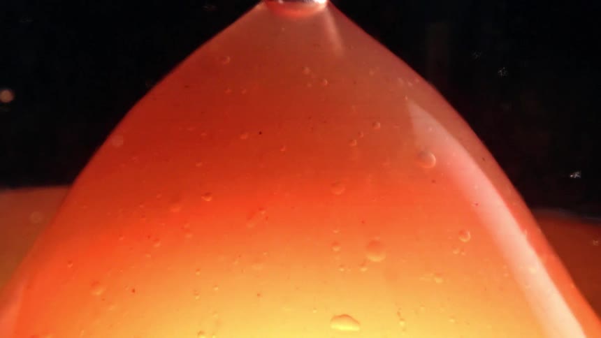 Orange liquid bubbling as more of it is poured in all happening in a dark moody atmosphere