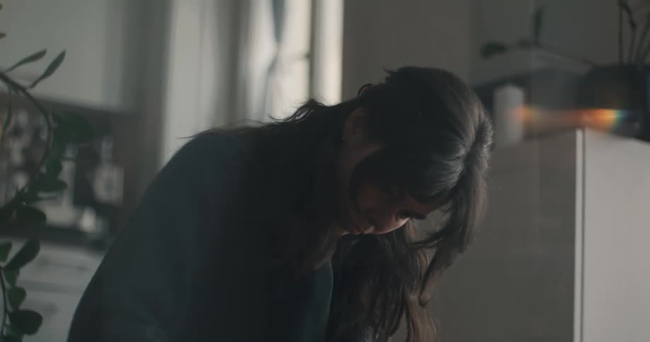 A woman with long dark hair wearing a charcoal sweater focuses intently as she uses both hands to press a thick white candle into a handmade pine wreath