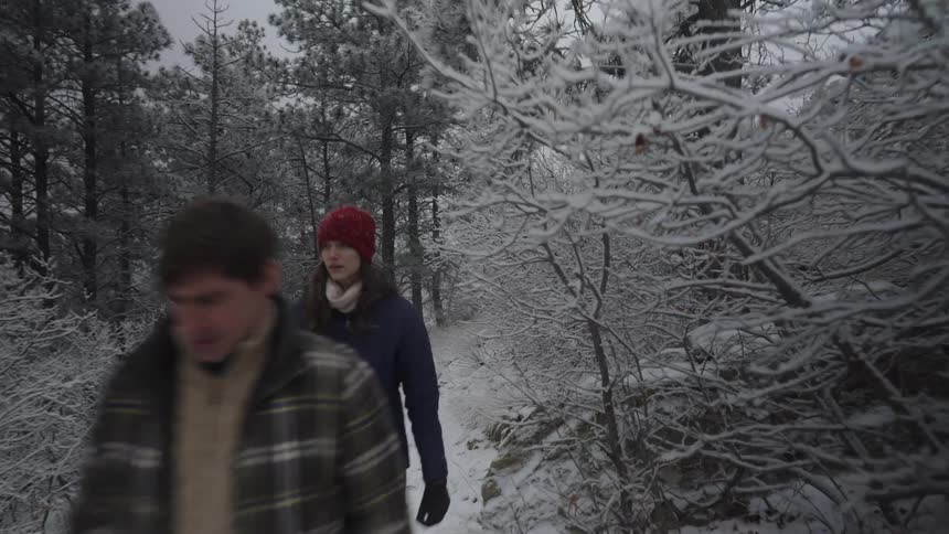 A young man and woman walking through a path in the woods during daytime