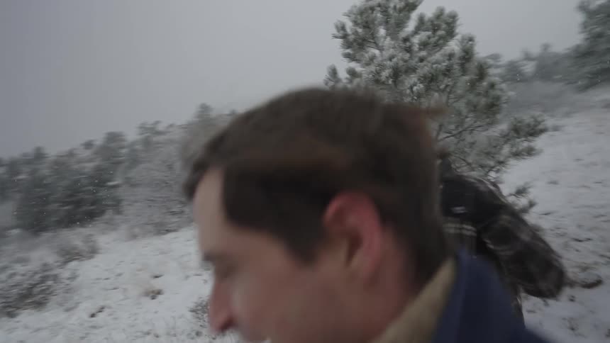 A couple walk together through a snowy forest landscape in winter