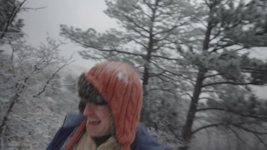 Friends smile while playfully running through the snow in the woods overlooking a valley on a winter day