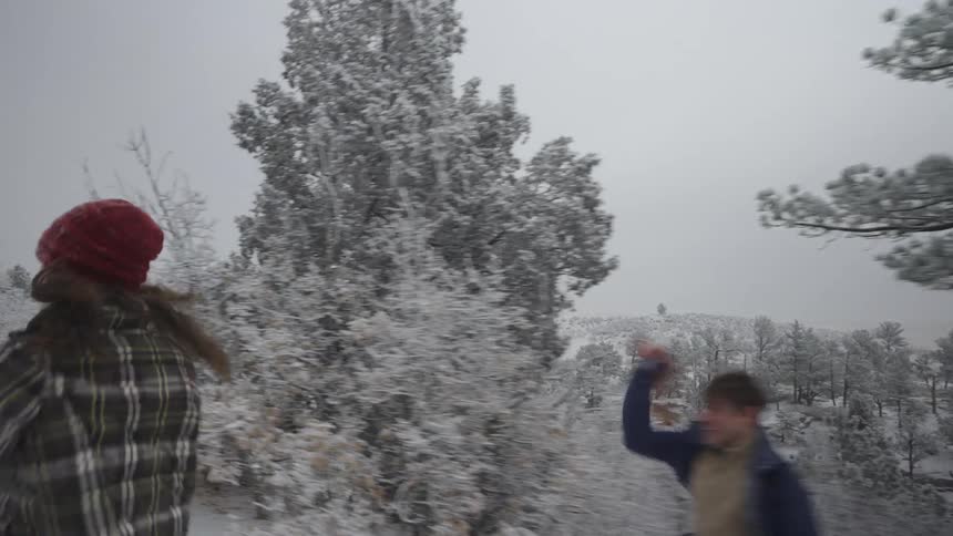 A female and a male run through a forest in a snowball fight with each other