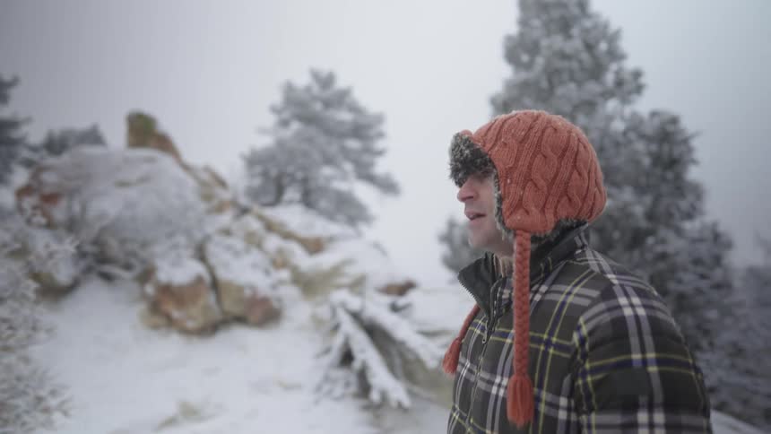 Man standing on a mountain with snow covered trees and rocks