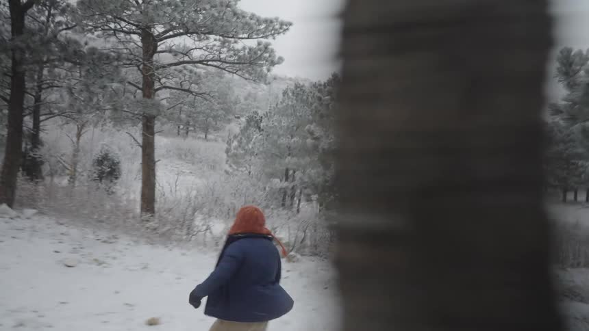 Young man running through a rural field knocking snow off trees on a winter day