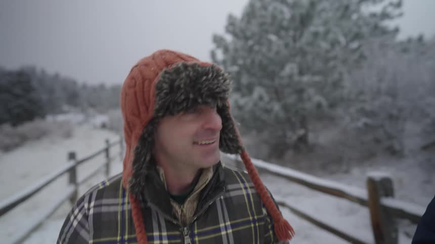 Two people walking along a snowcovered path with trees and fences around