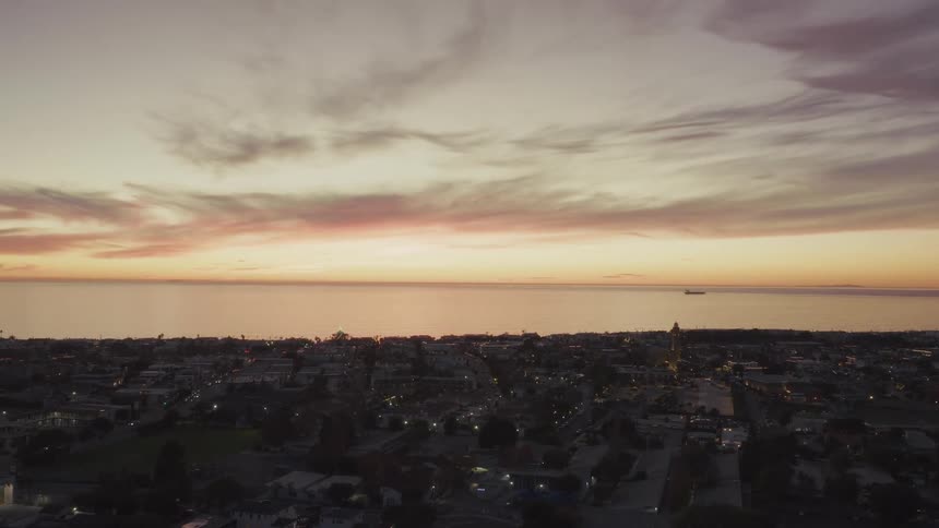Coastal cityscape at sunset with vibrant sky in shades of orange pink and purple over the ocean