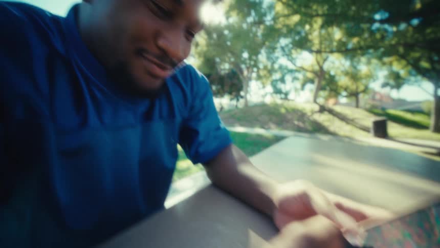 Man seated in a park using a smartphone with both hands under natural light
