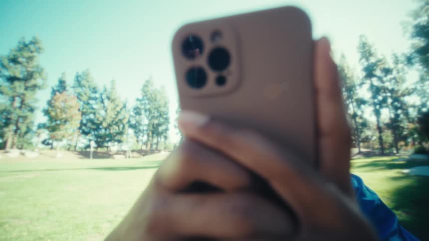 Man outdoors holding a smartphone with both hands in a park during daytime