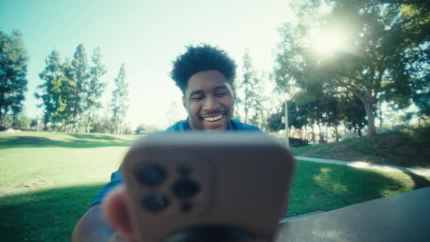 Man seated in a park holding a smartphone with both hands during daytime