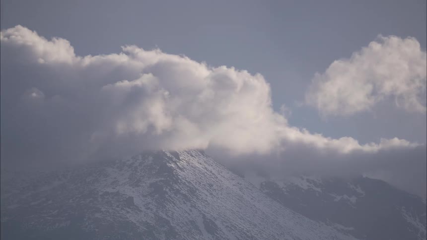 The top of a mountain with several white clouds passing by quickly