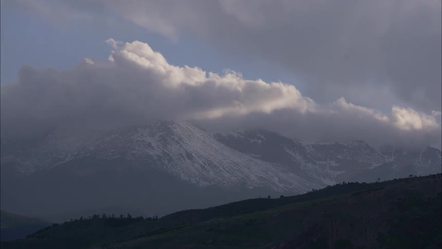 Mountain with cloudcovered peak and partially snowcovered slopes under a cloudy sky