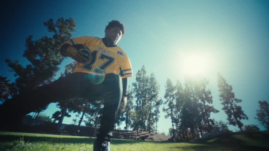 A man plays american football on a grassy field in a park under bright daylight