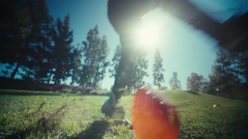 A football player intensely kicks a football on a sunny outdoor field