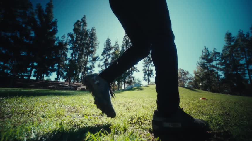 Athlete kicking a football on a sunny day standing on a green grass field and wearing a yellow jersey