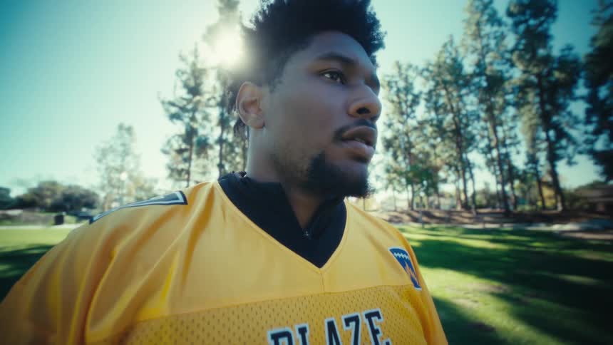 An american football player wearing a yellow blaze jersey with the number 17 stands in a sunny parkthe camera circles around him in a closeup shot as he looks off into the distance