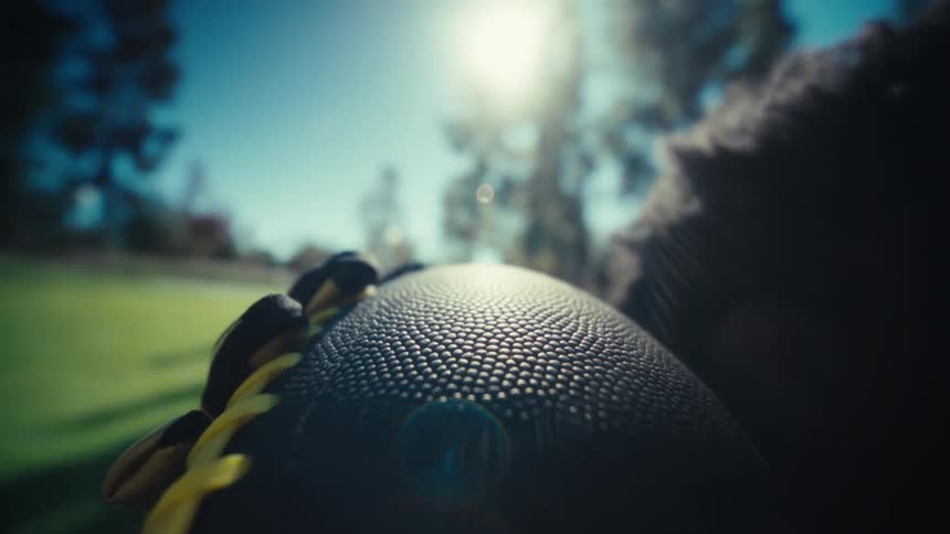 A football player throws an american football in a sunny park