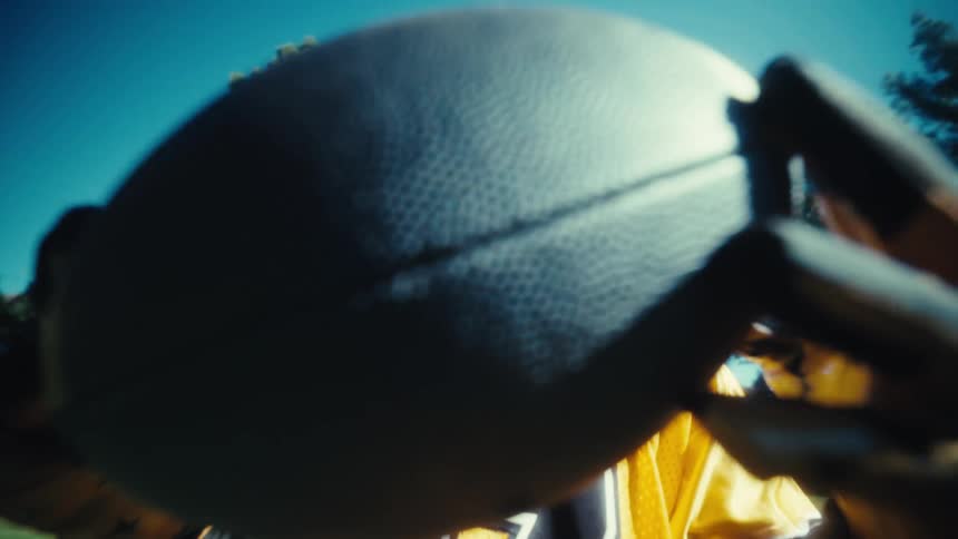 Young man wearing yellow gloves and a yellow jersey holding a rugby ball on a sunny day