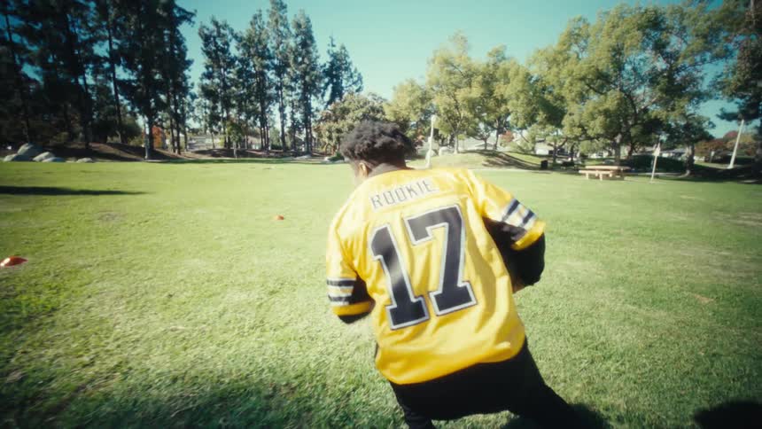 Man running on a grassy park field wearing a sports uniform during daytime
