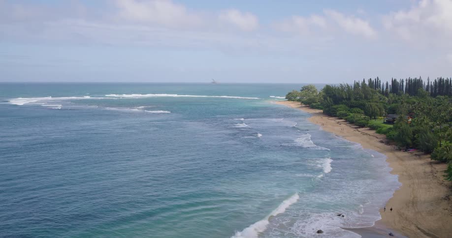 Tropical vegetation borders light sandy beach with gentle waves and houses among the trees