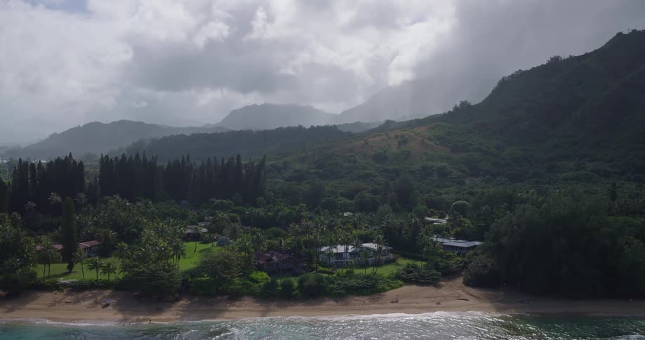 The camera pulls back over the ocean revealing a lush secluded coastal community nestled at the foot of misty treecovered mountains