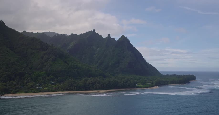 Aerial view of jagged mountains rising along a lush coastline with scattered homes by the ocean