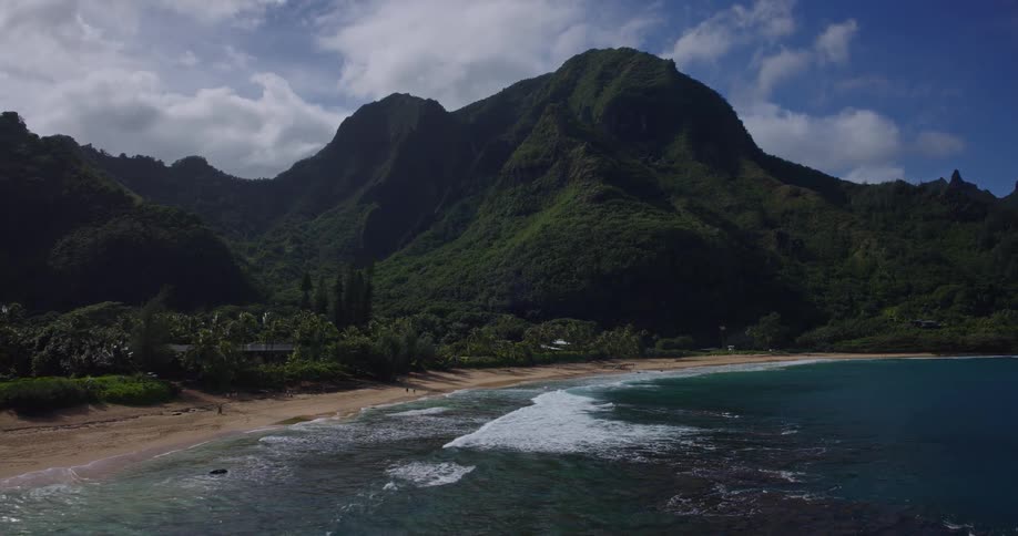 The waves hit the shore of the island with green mountains
