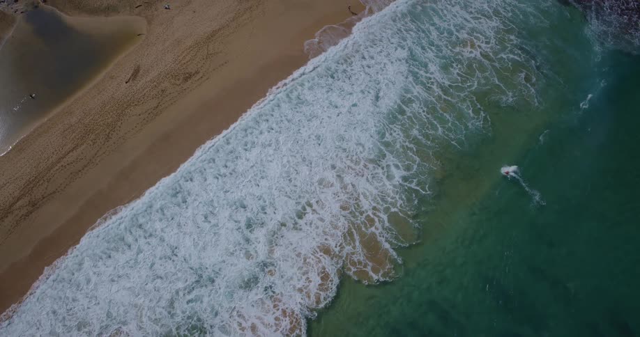 Aerial of a surfer riding an ocean wave into the sandy shore