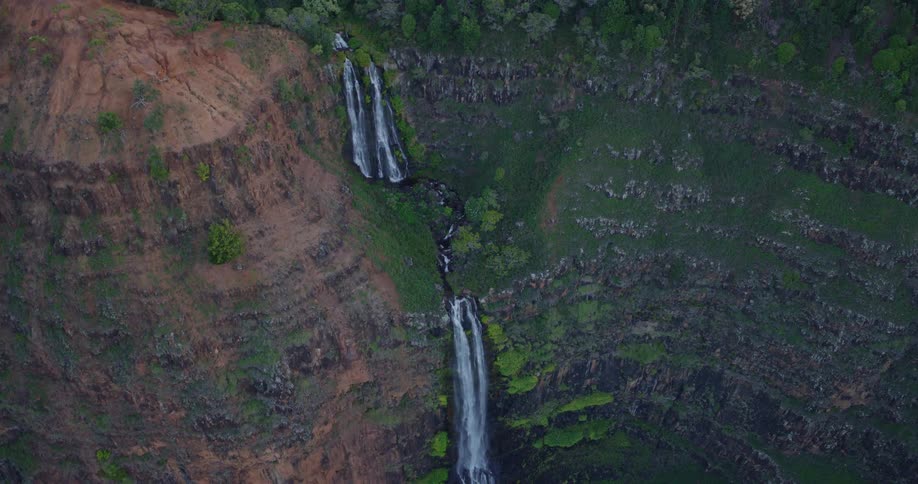 Multitiered waterfall flows through forested canyon with contrast between arid rocks and dense vegetation