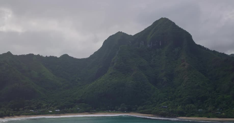 Forested mountains overlooking waves rolling in to shore and over a beach
