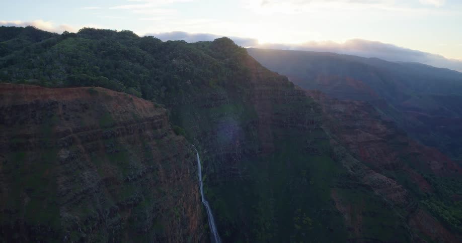 Natural landscape of a mountainous regious surrounded by valleys with a waterfall coming from one of the mountains outdoors during dusk or dawn