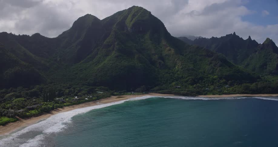 Aerial view of green mountains and serene ocean waves along a quiet tropical beach