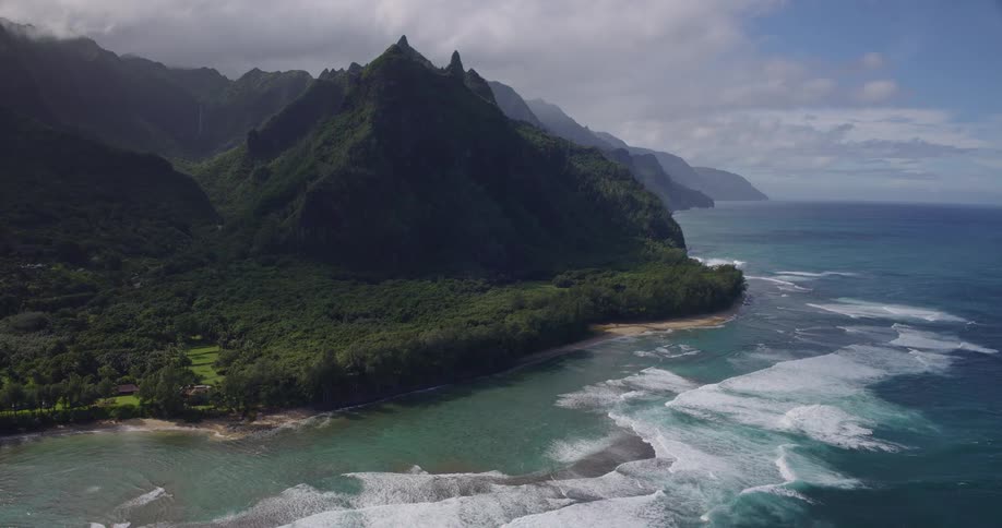 Lush coastal landscape with steep green mountains beside vibrant blue ocean and winding beaches