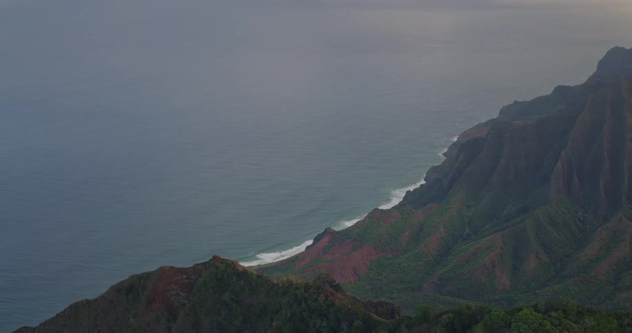 Dense vegetation covers steep cliffs descending to the ocean along a curving coastline