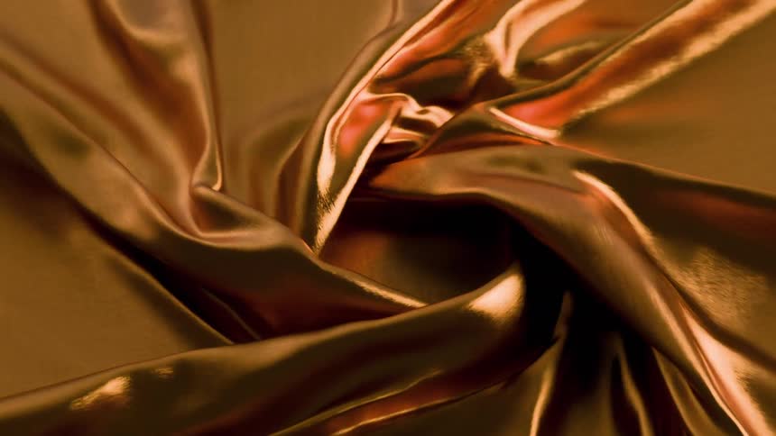 A shimmering goldenbrown fabric is shown swirling and gathering into a central roselike spiralthe metallic sheen reflects light across the deep folds and ridges as the material continues to shift and bunch together