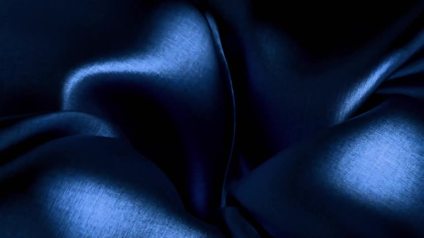 A shimmering dark blue fabric dramatically folds curls and unfurls into darkness catching sharp highlights on its metallic looking texture
