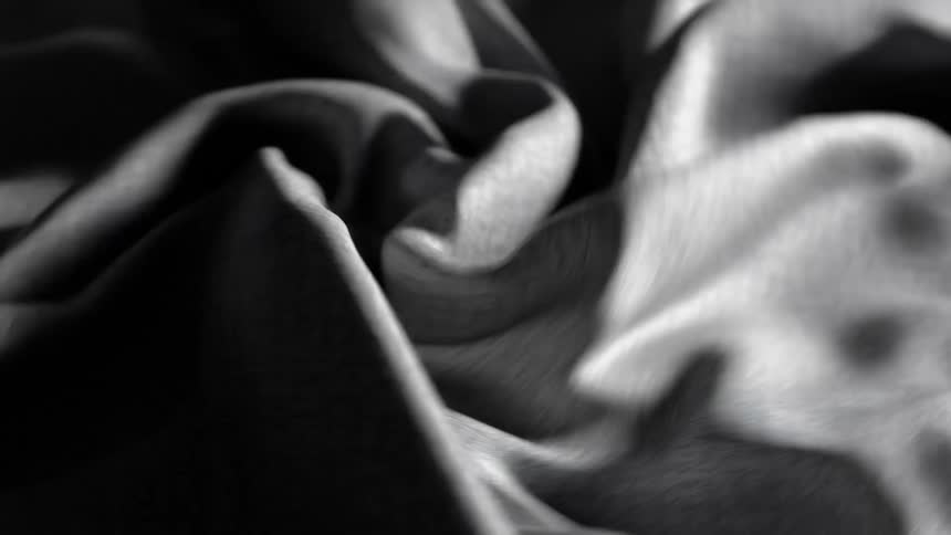 A piece of grey textured fabric begins to twist into a tight spiral before unwinding and rotating back and forth under highcontrast lighting that emphasizes the deep rhythmic folds and shadows