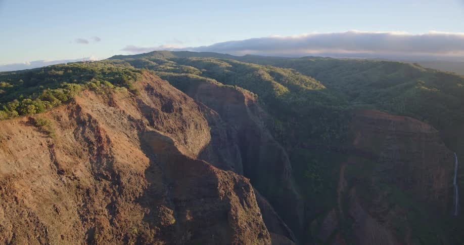 Aerial view of a vast green valley with a river winding through lush fields toward a dark blue ocean under a bright morning sun
