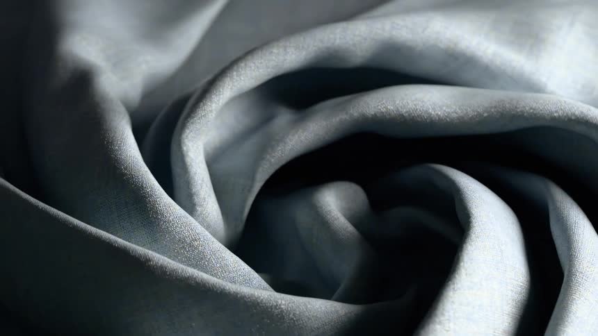 A smooth grey fabric is being swirled and bunched into a tight florallike spiralthe movement highlights the fine texture of the weave and the soft play of light across its shifting folds