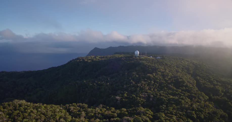 White observatory dome stands out among forested mountains overlooking the ocean