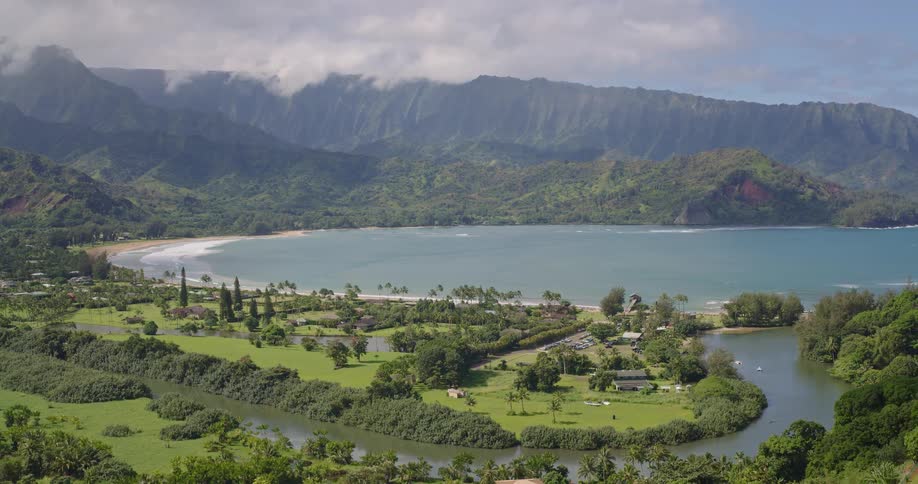 A scenic view shows a winding river green fields and houses leading to a bay with cloud covered mountains