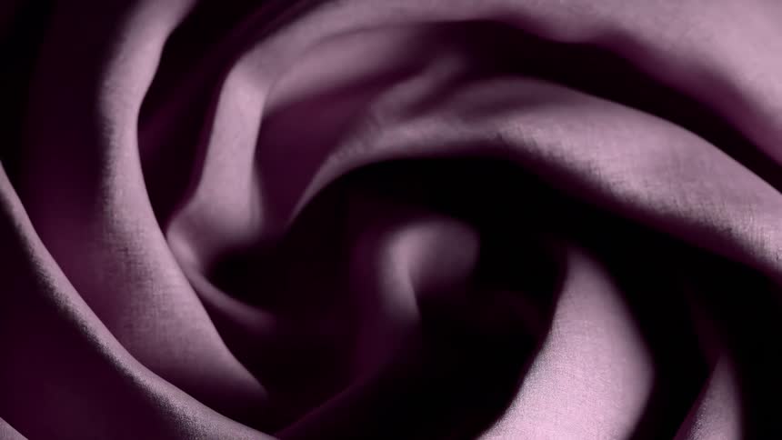 Dark pink fabric with a smooth texture ripples and swirls in a circular motion creating soft folds and shadows under gentle light
