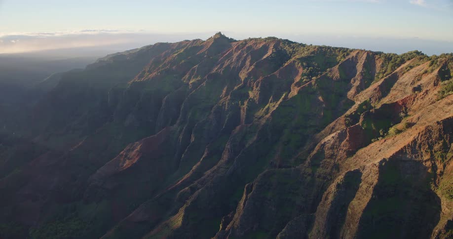 Jagged rock formations and deep valleys stretch across mountain range with sparse vegetation