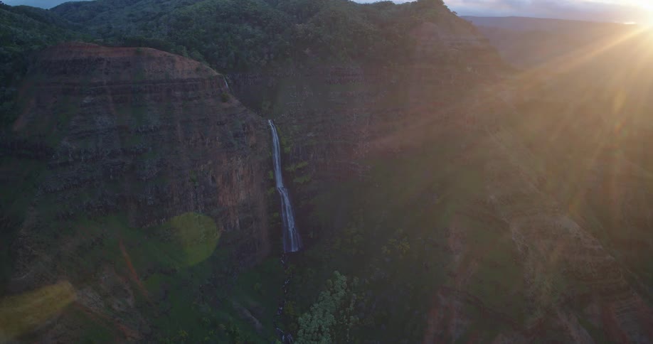 Mountain range glowing in the warm colors of sunset with a narrow stream flowing down a rocky slope