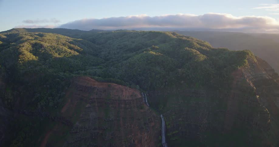 A narrow waterfall plunges over the cliff side of a green mountain