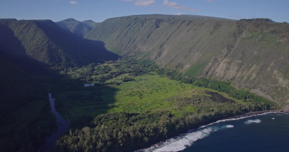 Aerial view of a lush green valley bordered by steep cliffs along the ocean coastline