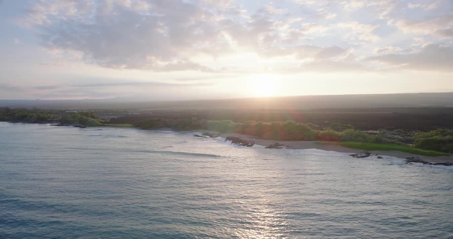 Aerial view of a tropical coastline with lush greenery and soft ocean waves at sunrise